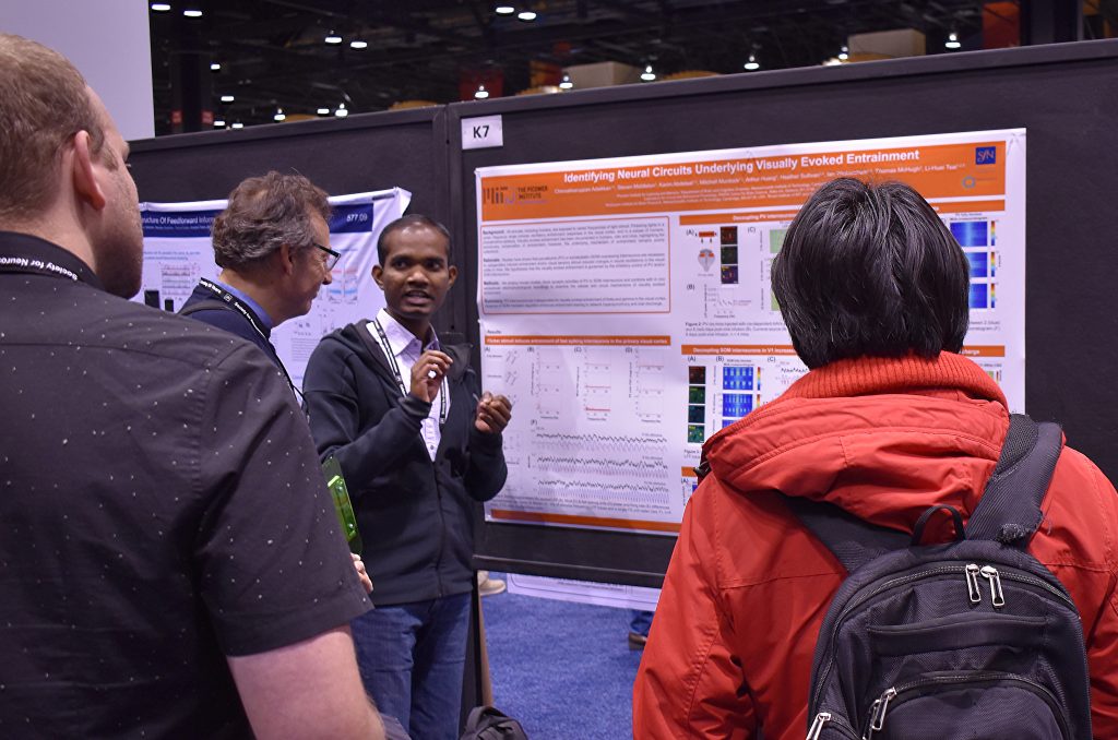 Chinna Adaikkan stands before a research poster and talks to two onlookers.